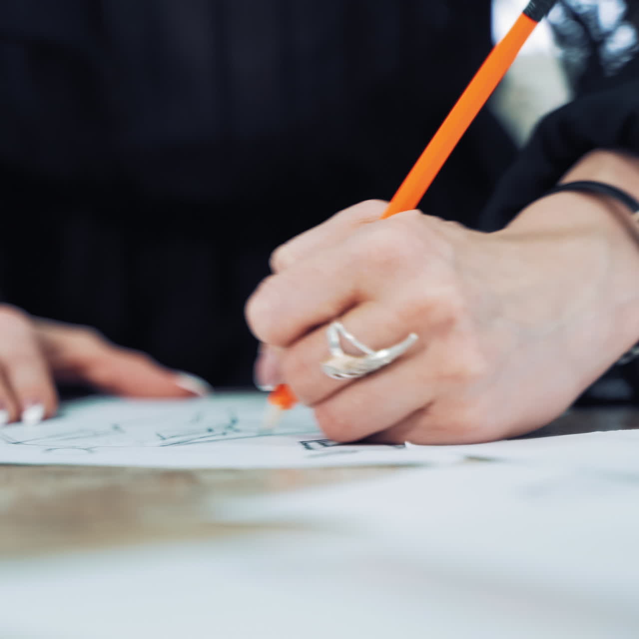 Hands of a professional tailor is drawing a sketch with a sharp pencil on a table. Dressmaker is making a creative design of a dress on a sheet of paper in her workplace.