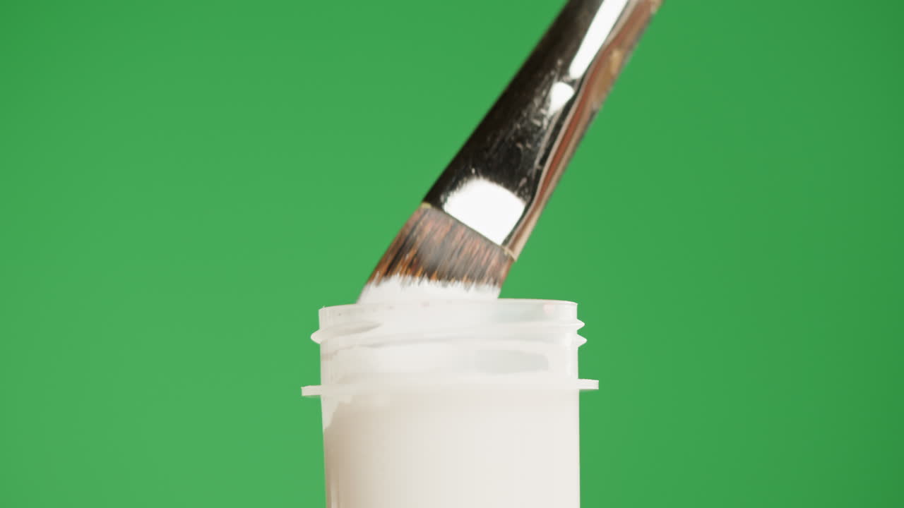 Nærbillede af pensel, der dypper ned i hvid maling og drypper