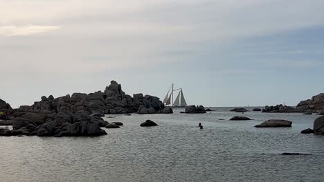 two-masted sailing ship crosses the scene at cala della chiesa spot on lavezzi island in corsica with people bathing, france