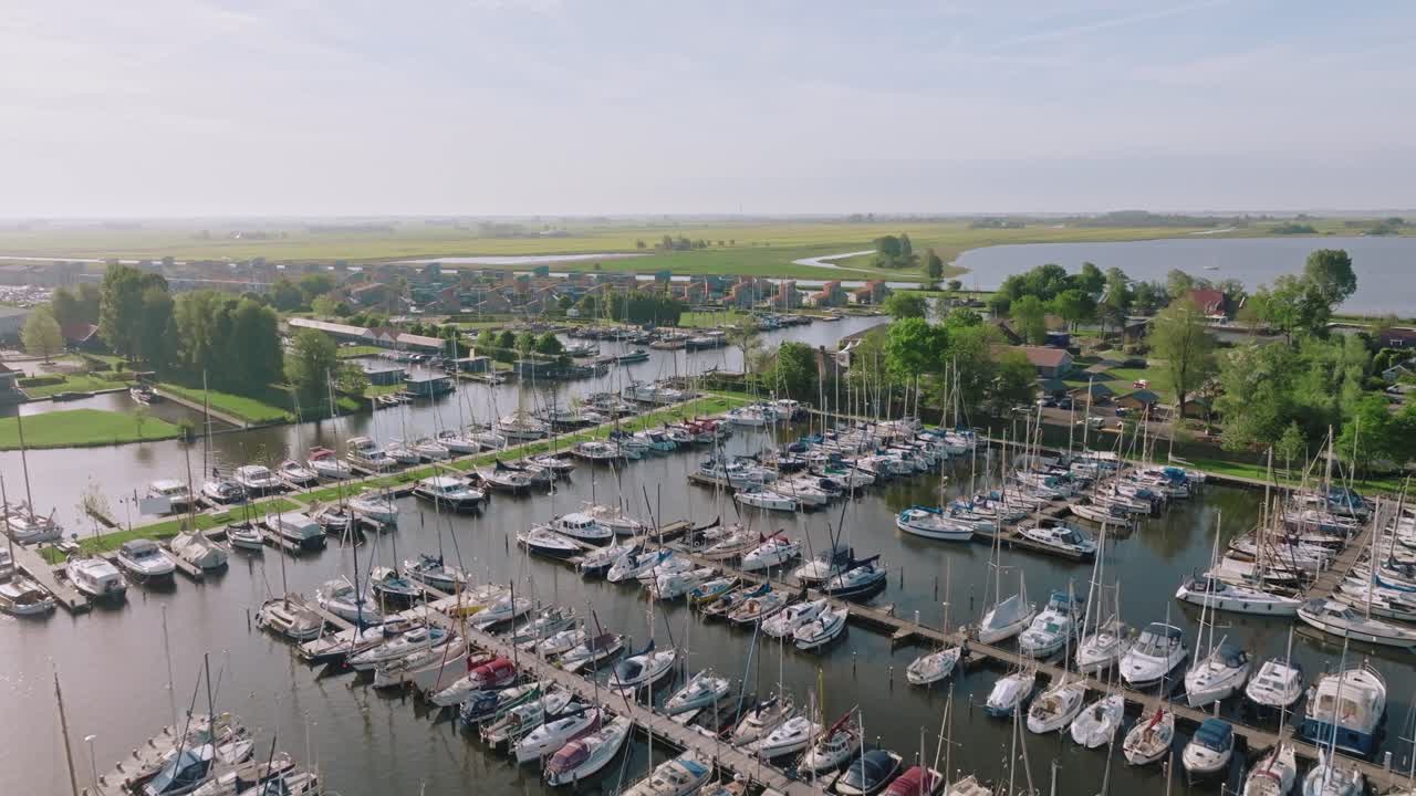 Zoom in aerial shot highlights numerous sailboats and peaceful waters of Heeg marina under soft daylight