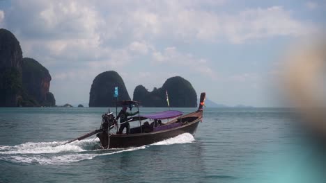 traditional thai boat sails at high speed away from a tourist attraction over a calm sea on a partly cloudy day