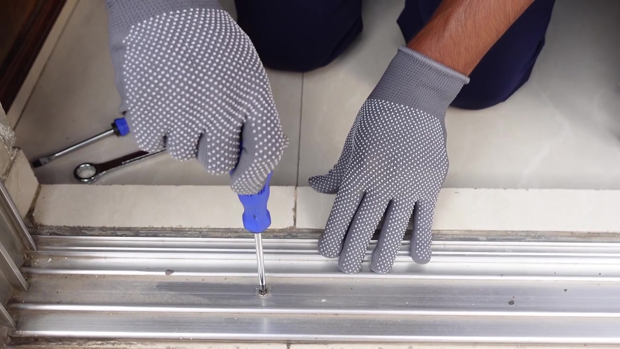 Person Wearing Protective Gloves Using Screwdriver on Metal Door Frame