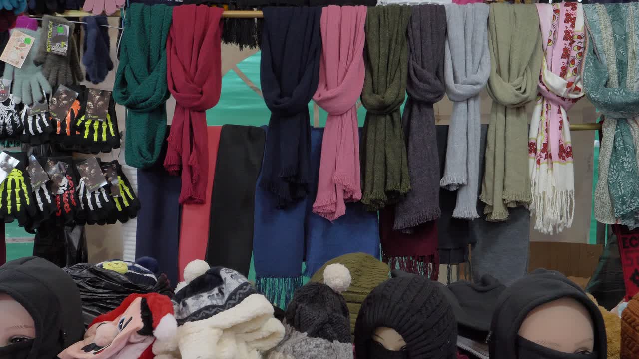 Ripresa panoramica di sciarpe e cappelli fatti a mano esposti su una bancarella nel mercato di Cuenca.