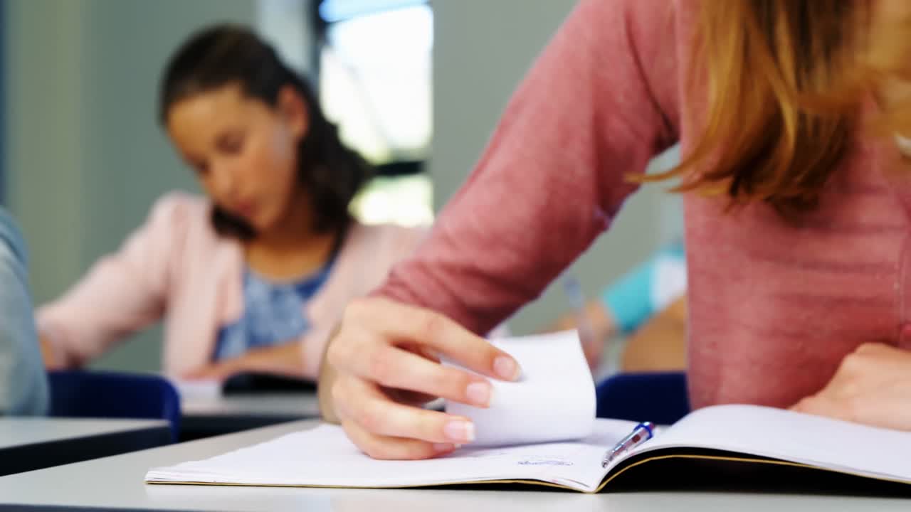 Skolepige sender en seddel til sin klassekammerat under eksamen i klasseværelset