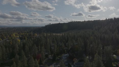 Wooded-suburban-neighborhood-with-beautiful-cloudy-sky-and-wooded-hillside-in-the-distance,-aerial-footage