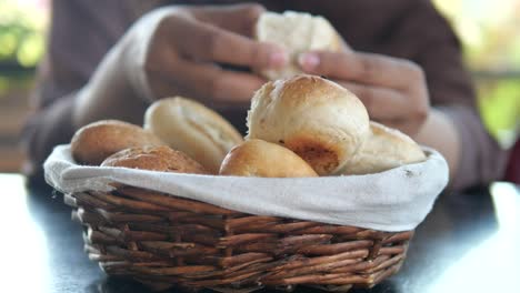 a person's hands holding a warm bread roll from a basket of bread rolls