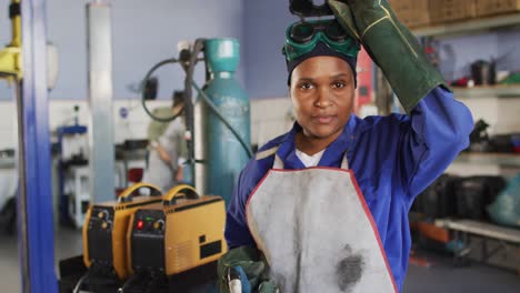 Video-of-african-american-female-car-mechanic,-taking-off-mask,-looking-at-camera