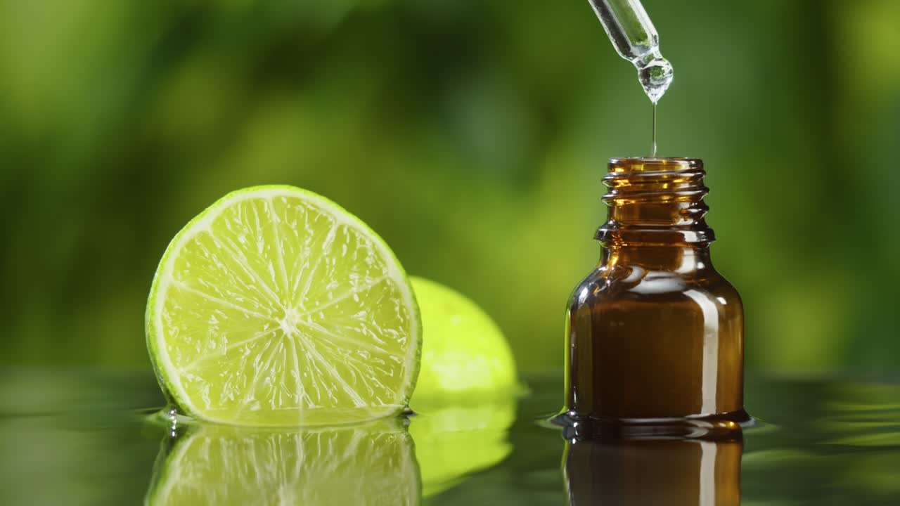 Dripping oil from pipette into bottle close-up, lime juice. Making aroma serum on green background. Dropping liquid citrus extract, skincare routine, treatment spa concept. Traditional medicine