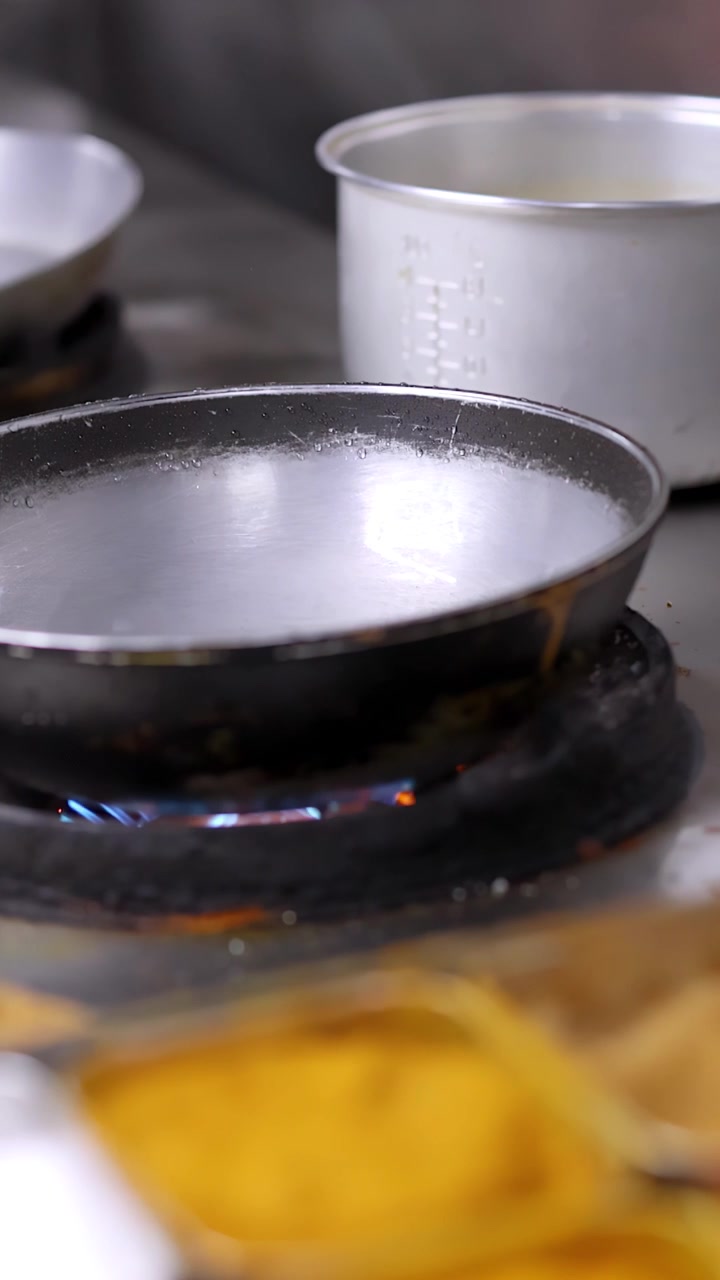 Static close-up shot of a frying pan heating over a blue gas flame in kitchen.