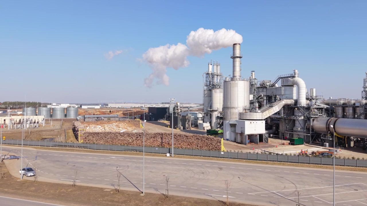 Aerial Processing Plant With Tall Chimney And Nearby Storage Piles, Road Frontage And Industrial Conveyors Visible, Daytime Footage Highlighting Material Handling And Emission Stack