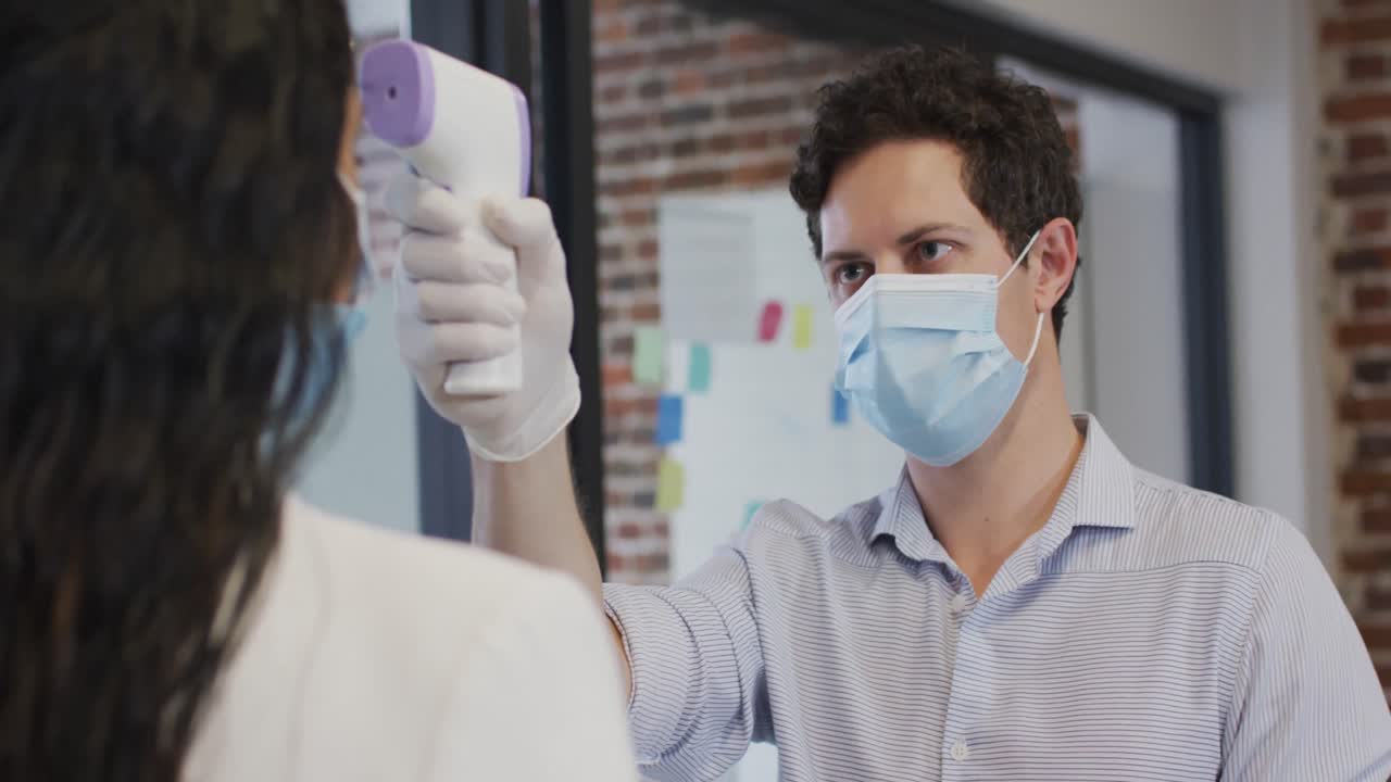 Uomo con mascherina che controlla la temperatura di una donna in ufficio.
