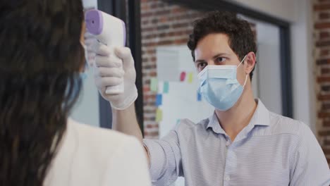 man wearing face mask checking temperature of woman at office