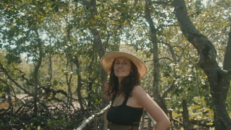 slow motion shot of a happy brunette european woman wearing a straw hat on a wooden bridge in an exotic forest