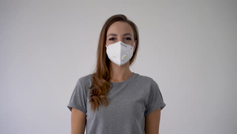 Woman-showing-thumb-up-and-pointing-her-medical-face-mask.-Copy-space-and-white-background.