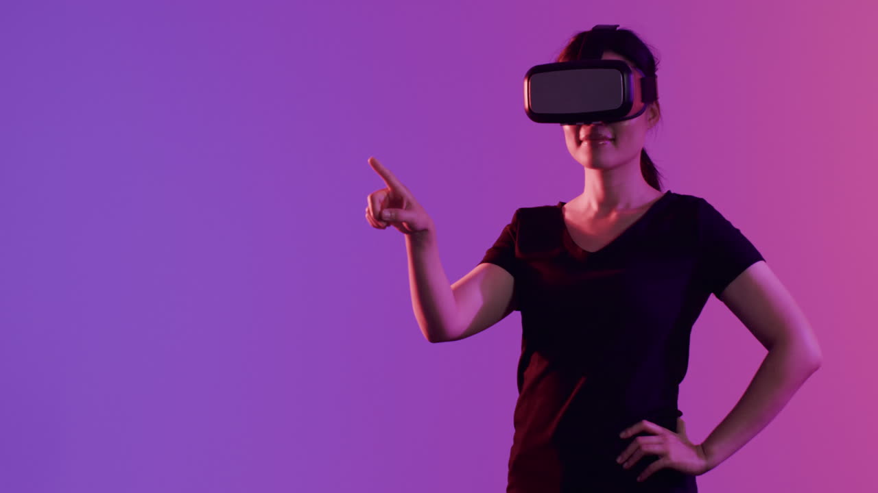 Asian woman using vr headset, touching screen on purple background, copy space, slow motion