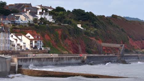 Wellen-Schlagen-In-Dawlish-In-Devon,-Großbritannien,-Gegen-Die-Ufermauer,-Während-Ein-GWR-Schnellzug-Entlang-Der-Roten-Klippenküste-Fährt