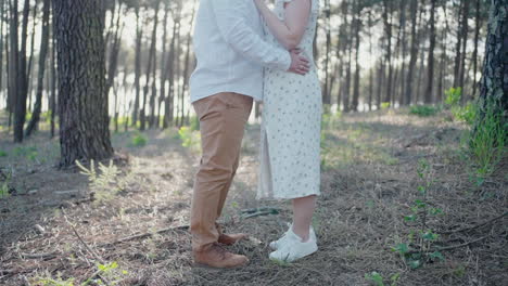 Couple-standing-close-in-a-forest,-focus-on-lower-body-and-legs,-with-sunlight-filtering-through-trees