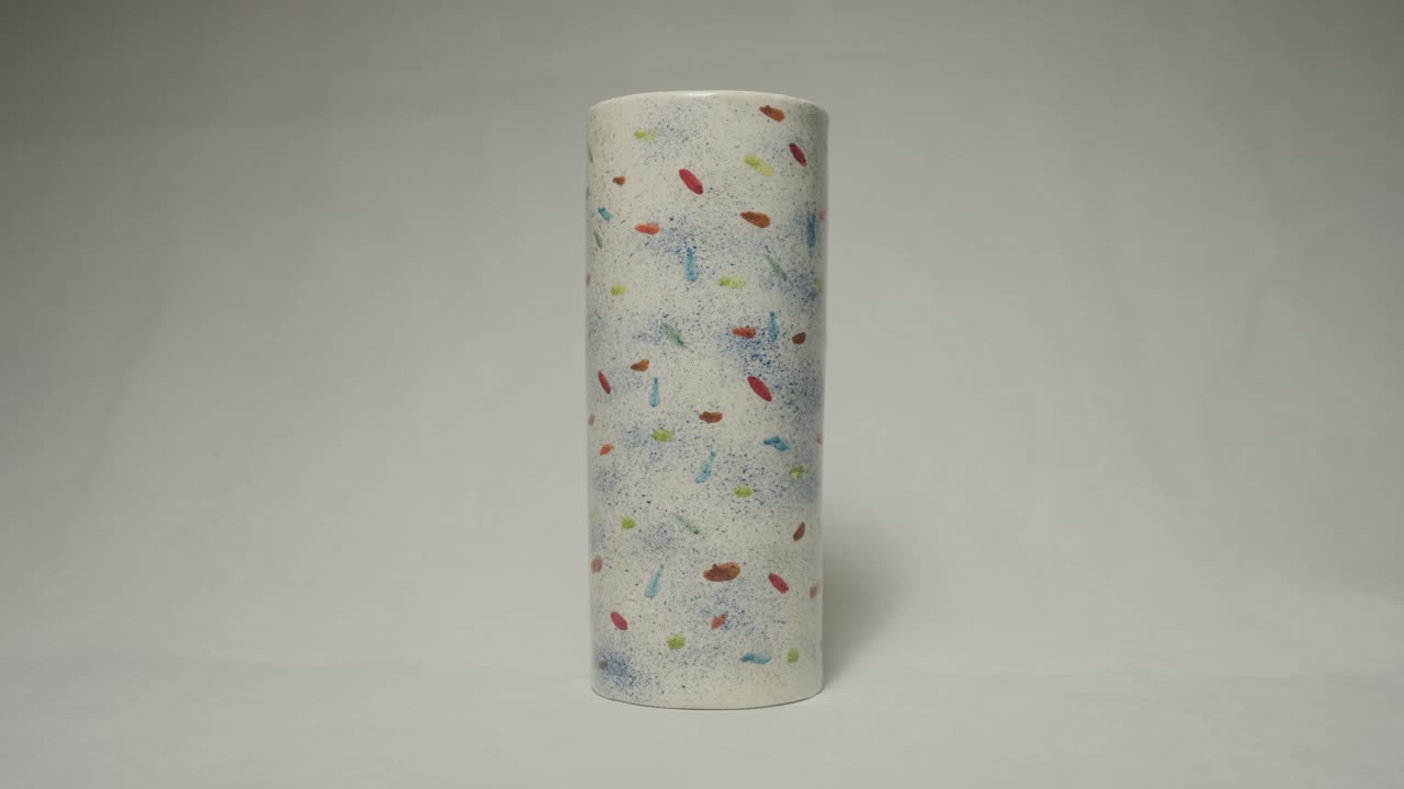 Static shot shows tall cylindrical ceramic vase decorated with hand-painted colorful abstract patterns, placed on clean white background to emphasize texture and artistic details