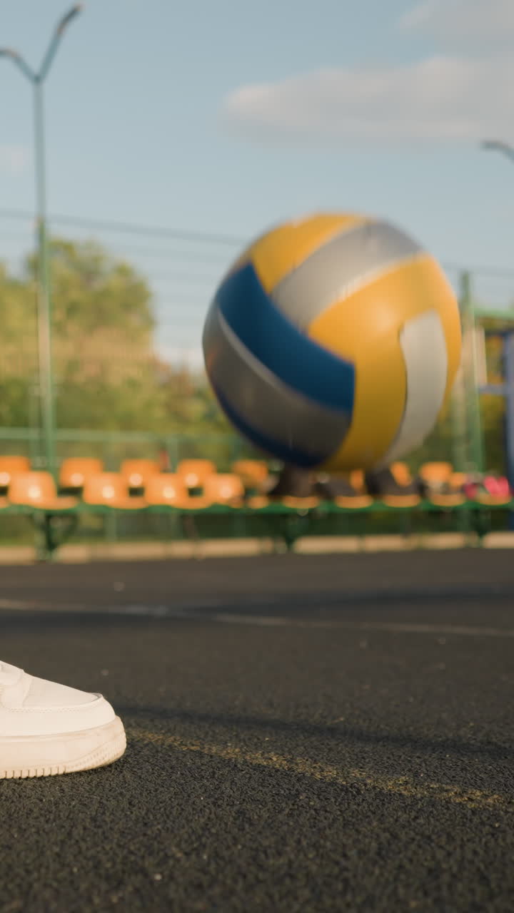 Side view of woman legs in green leggings bouncing volleyball outdoors with seating area and trees in background, showcasing active lifestyle and athletic energy in vibrant urban setting