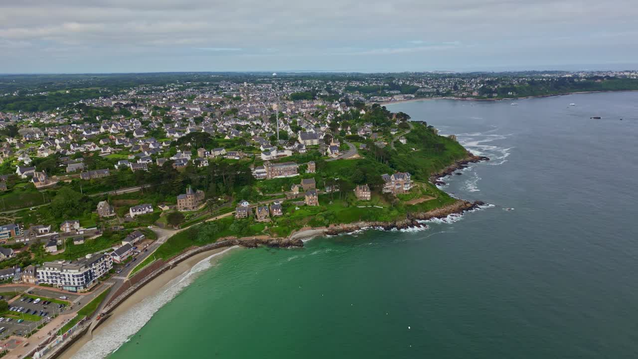 Forward drone movement at the Trestrignel beach at the coastal settlement with sweeping seafront and houses, Perros-Guirec, Brittany, France.