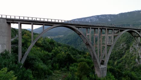 volando por debajo y a través del puente durdevica tara girando para revelar todo el puente en la noche oscura en montenegro europa rodeado de bosque y montañas