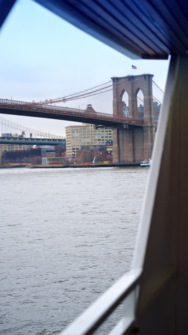Vista del Ponte di Brooklyn dal telaio di un traghetto sull'East River. Storico ponte sospeso in pietra visto attraverso la struttura di un'imbarcazione sotto un cielo coperto a New York City.