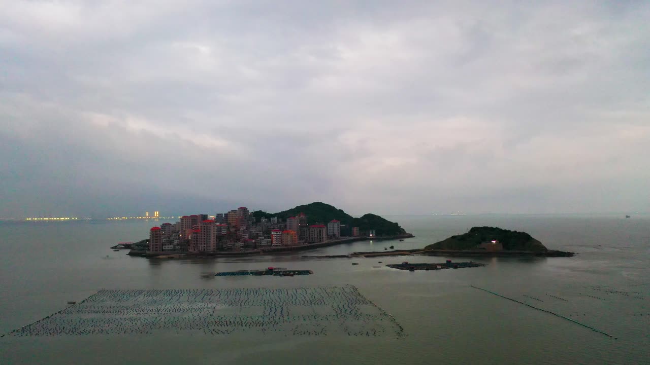 Drone orbiting around Gaobei Island in Fujian Province, China, at dusk. Densely populated island with skyscrapers.