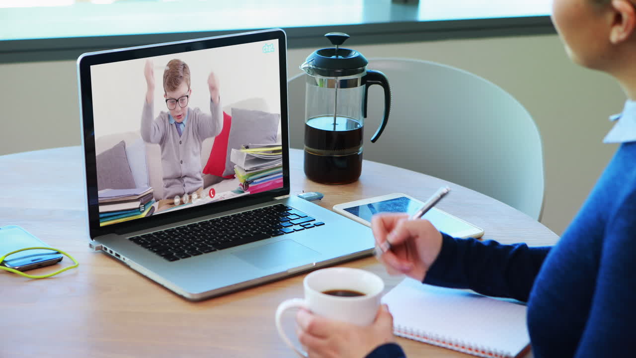 Caucasian female teacher using laptop on video call with schoolboy, making notes