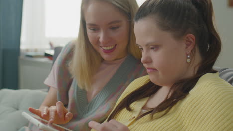 woman and girl with down syndrome using tablet and talking