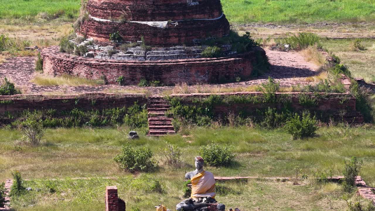 La videocamera di un drone si inclina verso l'alto da una statua di Buddha per rivelare antichi stupa e il paesaggio del villaggio