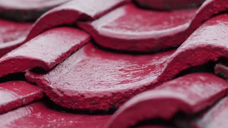 Rain-falling-on-red-roof-tiles-in-slow-motion,-capturing-the-glossy-surface-and-texture