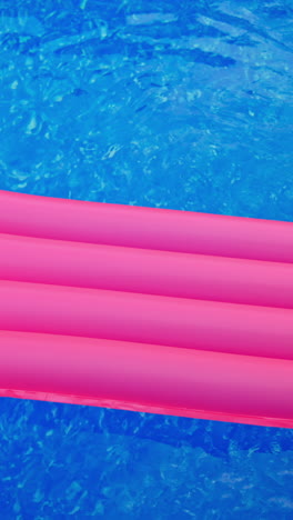 pink swimming mattress moving by the pink surface of water. inflatable mattress in the swimming pool. top view. vertical video