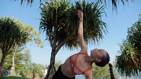 yogui en la alfombra practicando tablón lateral en la rodilla y extendiendo el brazo por encima - árboles pandanus en burleigh hill cerca de la playa - costa dorada, qld, australia