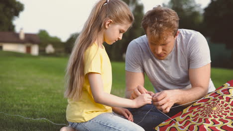 father and daughter fixing kite sitting on a green grass in the park 1