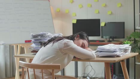 vista trasera de una mujer asiática durmiendo mientras trabaja duro con documentos en la oficina