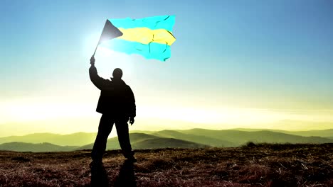 successful silhouette man winner waving bahamas flag on top of the mountain peak. cinemagraph loop background