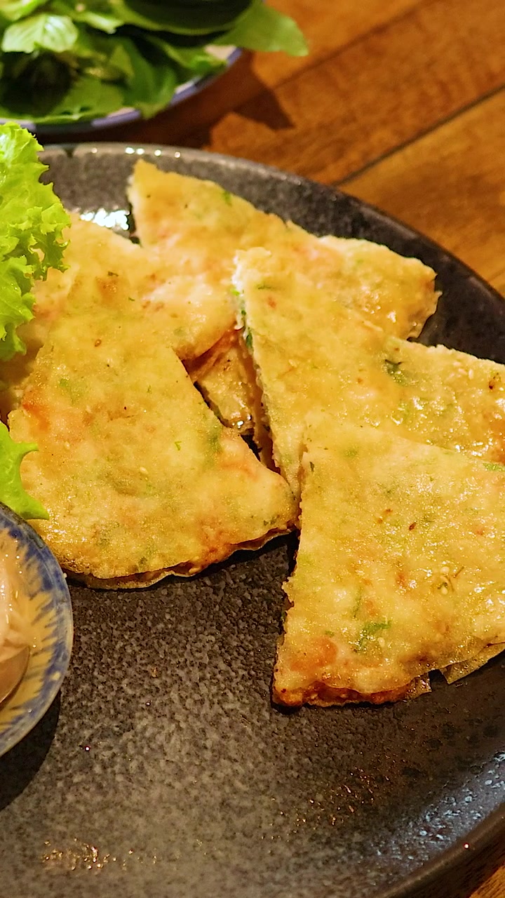 Una mano prende una croccante frittella vietnamita di gamberi da un piatto, mettendo in risalto texture e colori vivaci in un accogliente ambiente da ristorante.