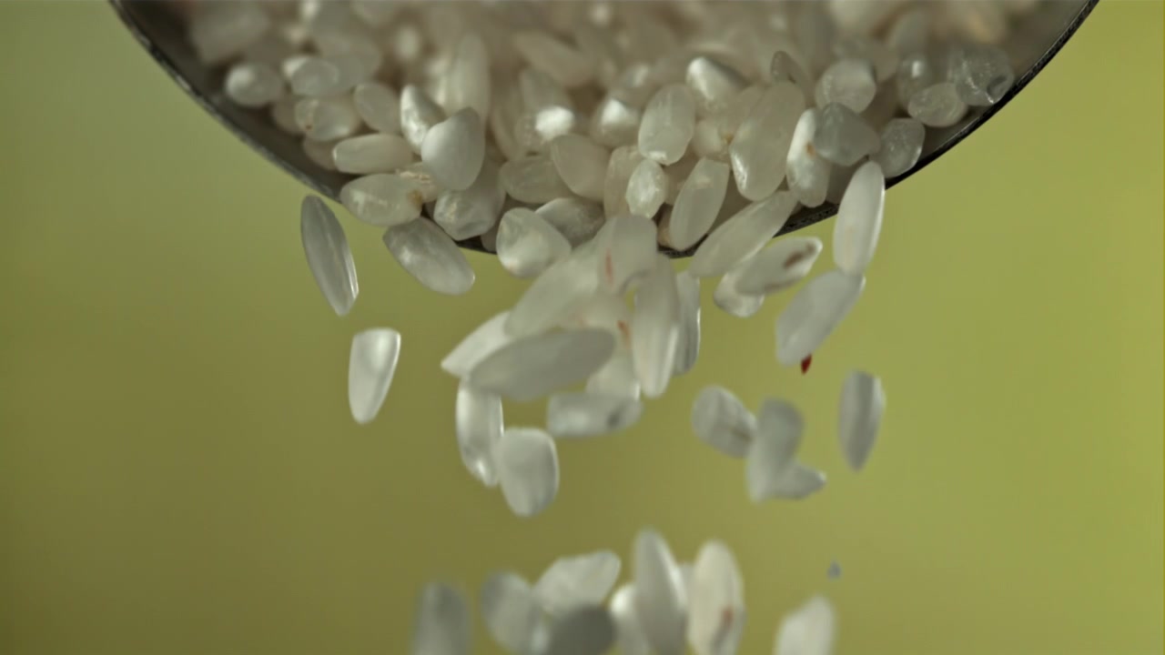 Chicchi di riso bianco che cadono da un cucchiaio al rallentatore