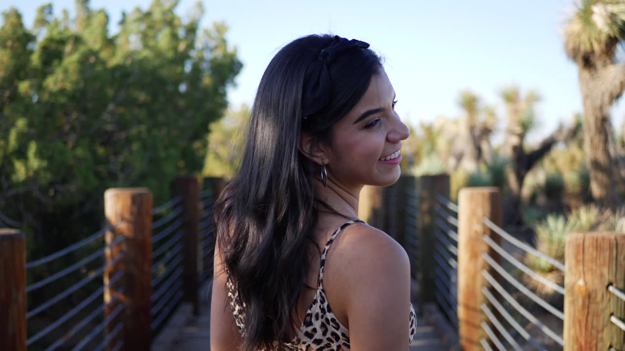 una hermosa joven hispana caminando y sonriendo en un sendero natural en cámara lenta a la luz del atardecer