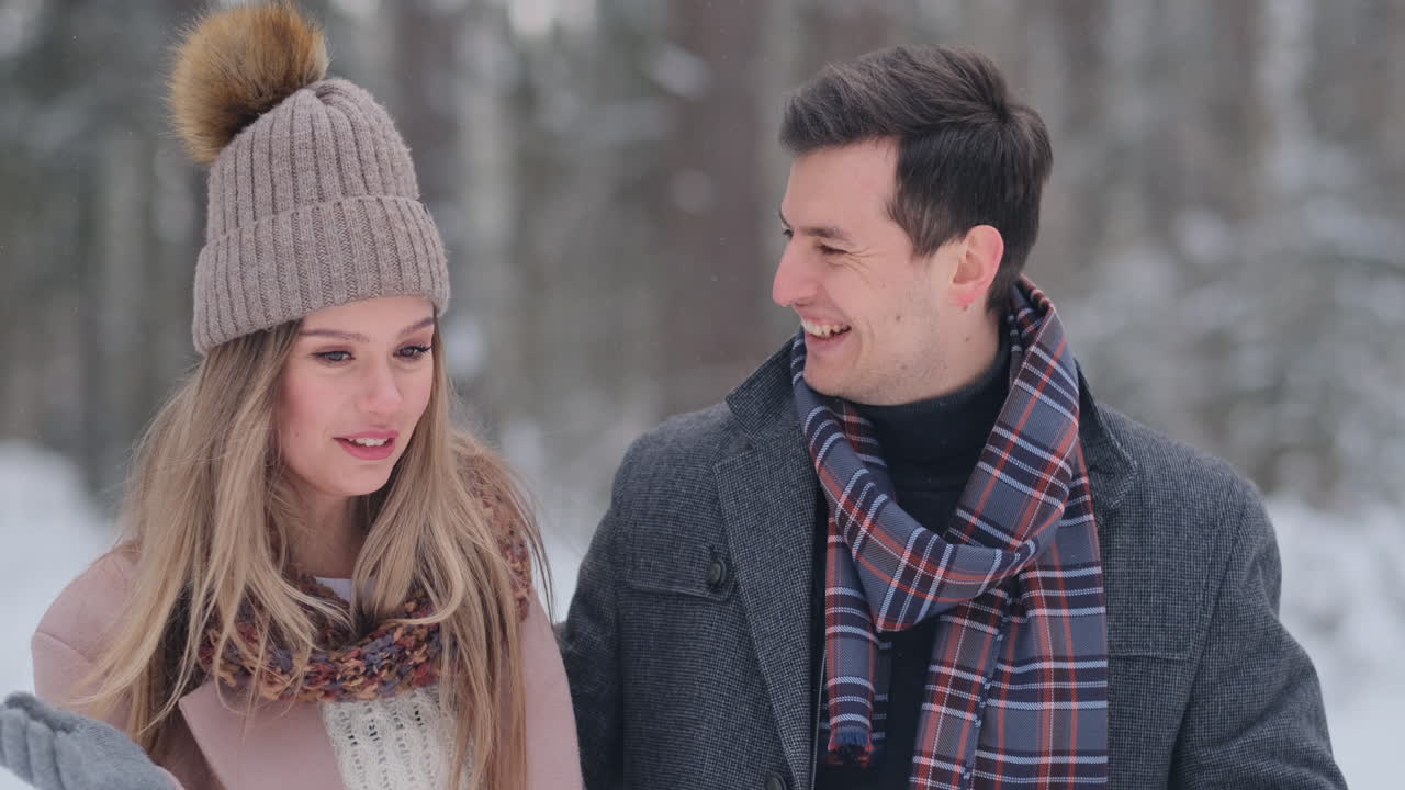 Young married couple in love walking in the winter forest. A man and a woman look at each other laughing and smiling in slow motion. Valentine's Day love story.