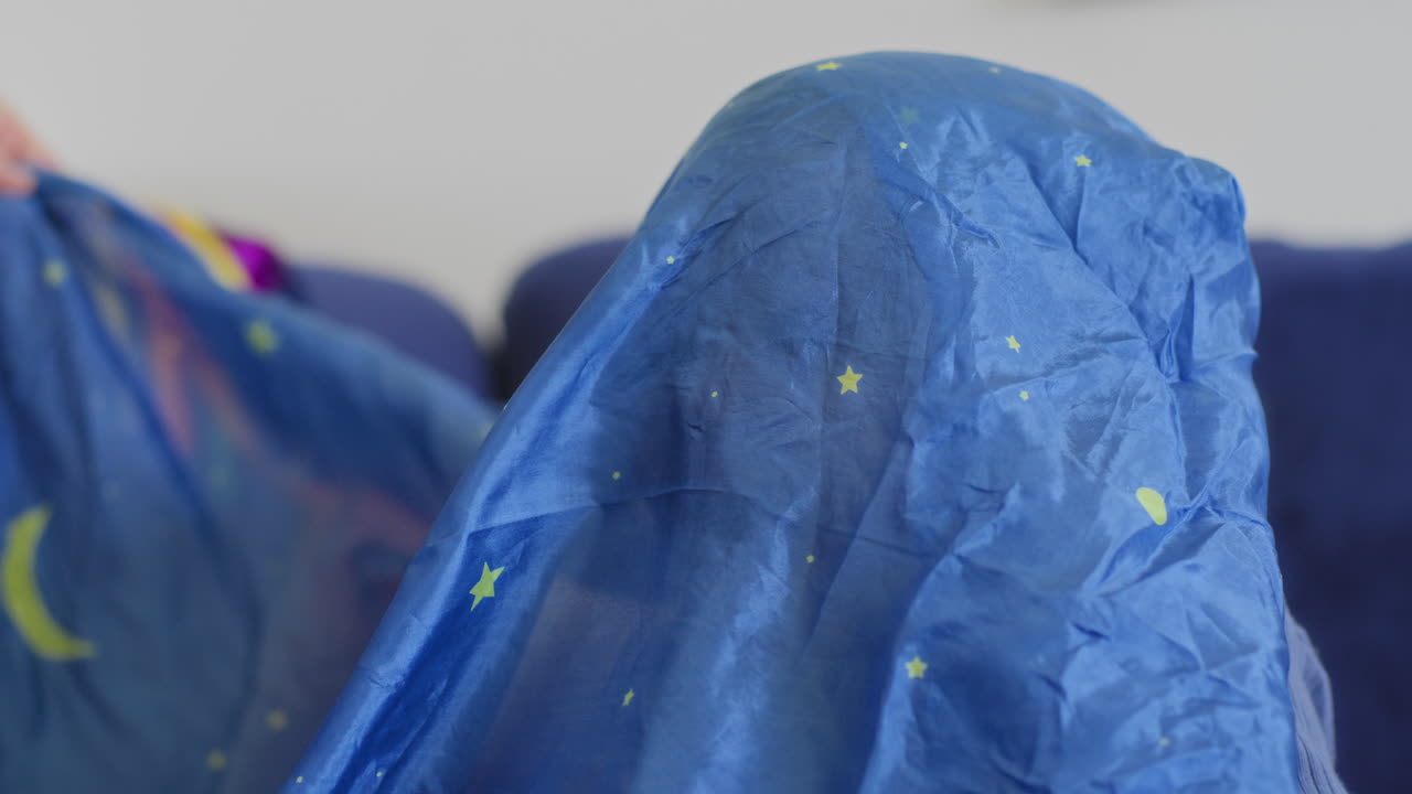 아기가 미소 짓고 웃으며 느린 동작으로 노란색 별과 함께 파란색 실크로 놀고 있습니다.