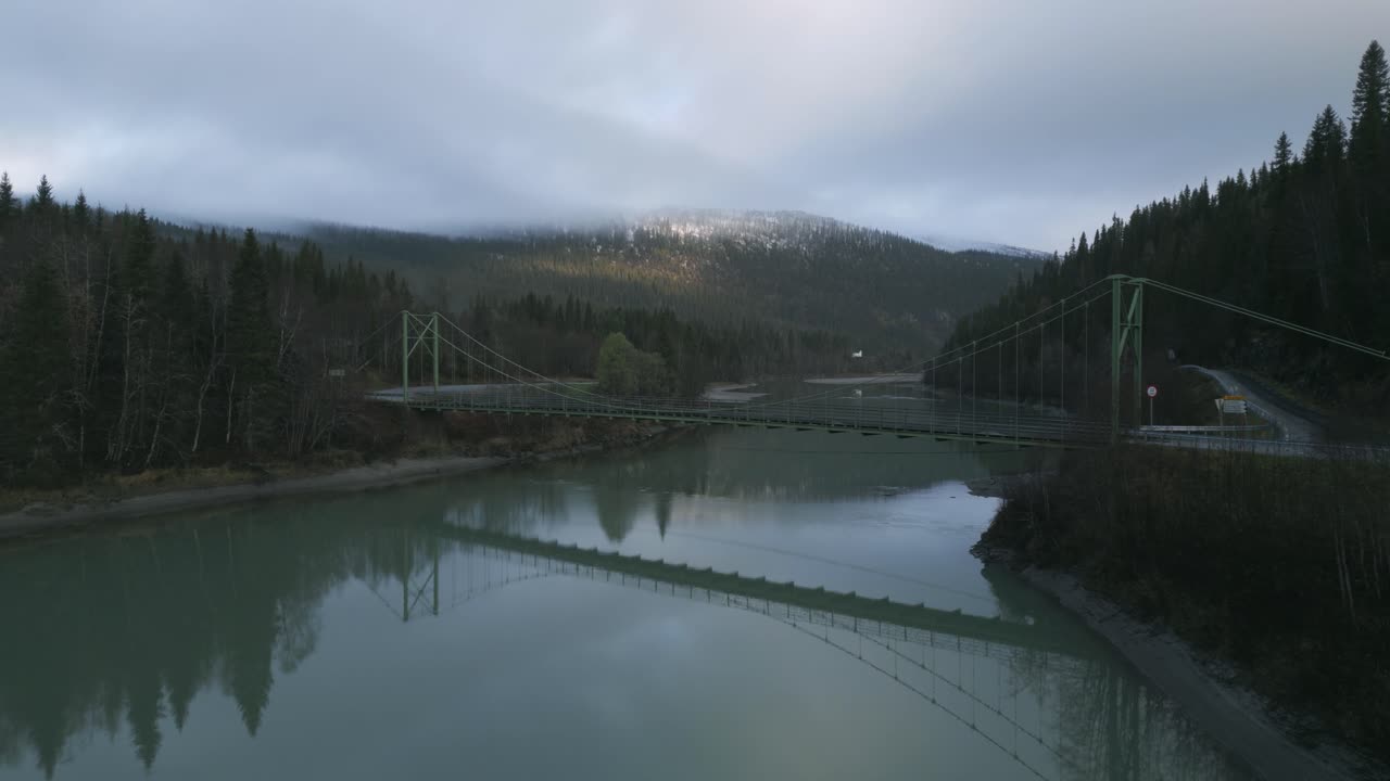 puente colgante sobre el río rovassaga en noruega con bosque y montaña como telón de fondo, iluminación al anochecer