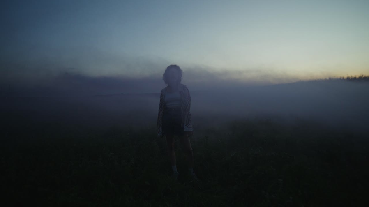 Woman in a field shrouded in fog at sunset