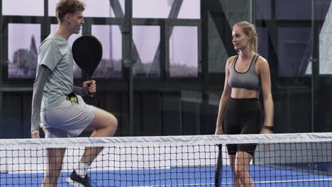 Young man and woman playing padel tennis on indoor court, enjoying competitive match with smiles