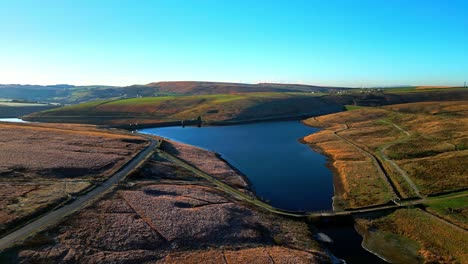 Weitläufige-Luftaufnahmen,-Die-über-Goldene-Moorlandschaften-Fliegen,-Die-Mit-Frost-übersät-Sind,-Direkt-Auf-Einen-See-Zu,-Ein-Stausee-In-Der-Ferne