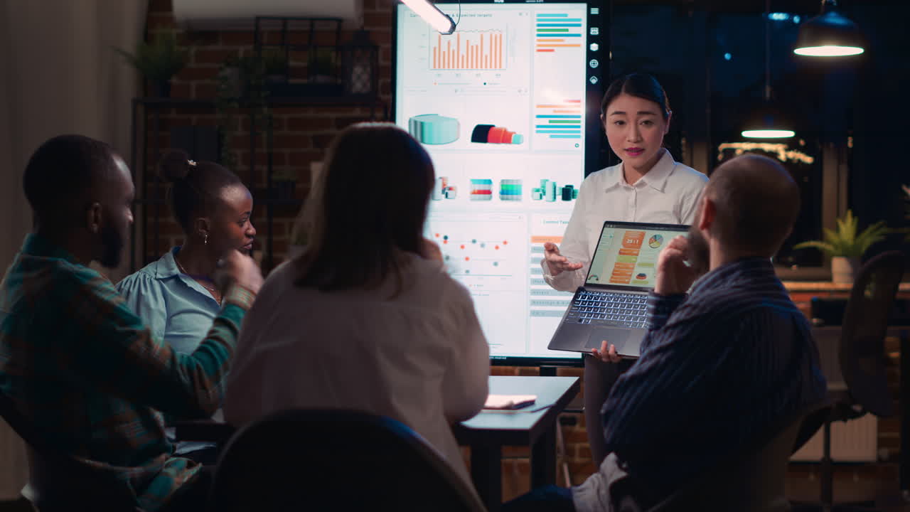 Asian employee presenting revenue report, showing charts on laptop