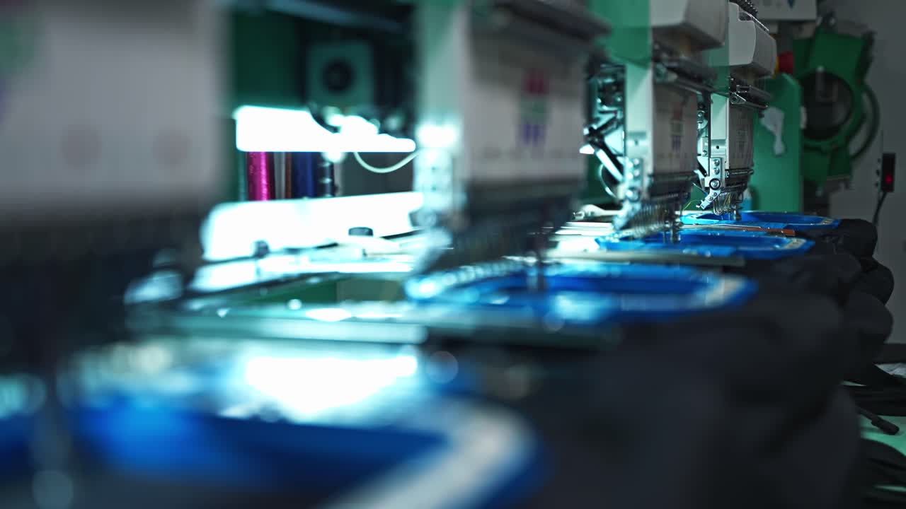 Closeup of embroidery machine with threads stitching precise patterns, slow motion unison of manufacturing operation