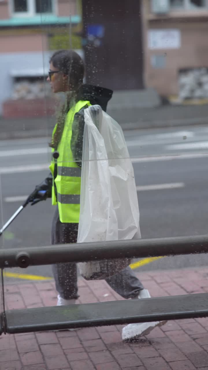 mujer limpiando una parada de autobús en la lluvia