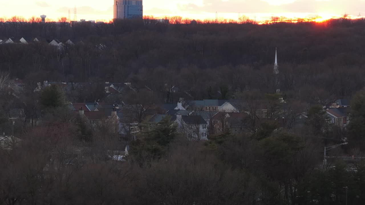 Luftfoto af Laurel Maryland ved solnedgang med vintertræer, boliger, kirketårn og et fjerntliggende kontortårn, der gløder i varmt aftenlys. Stigende vidvinkeloptagelse