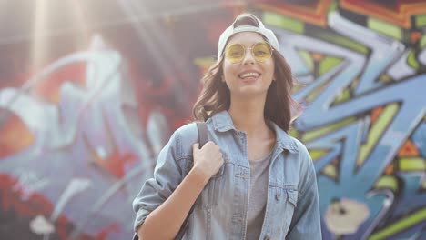 retrato de una joven hipster con estilo caucásica parada en la pared de graffity y sonriendo a la cámara